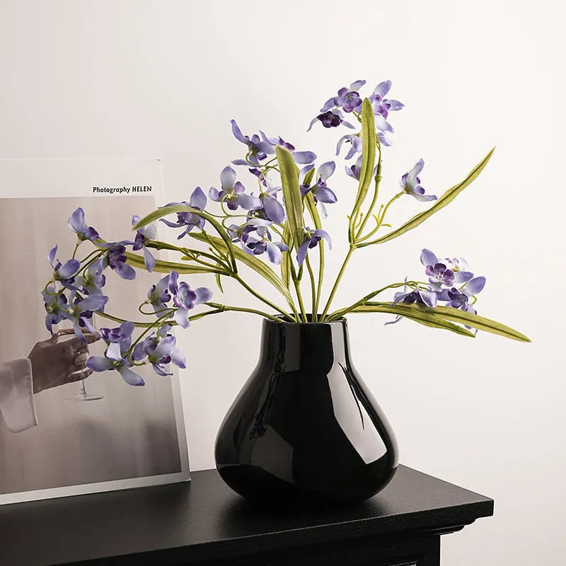 Black ceramic round belly French decorative vase with artificial flower stems on wooden surface