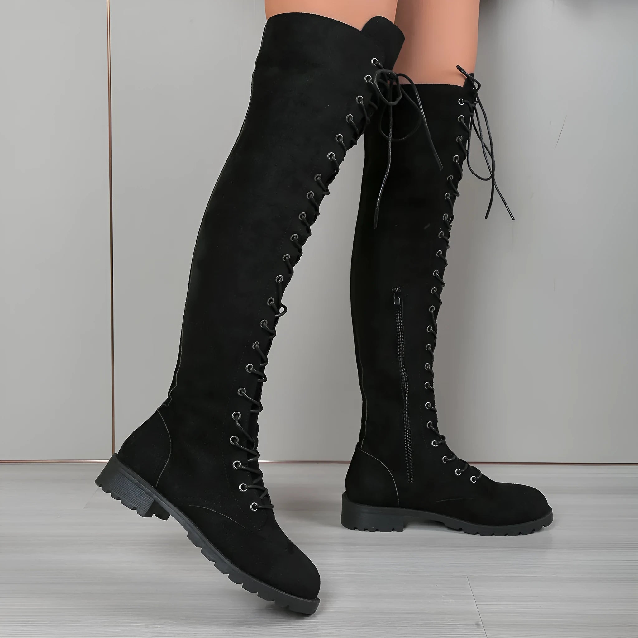 Black lace-up over-the-knee boots with round toe and flat rubber sole on a neutral background