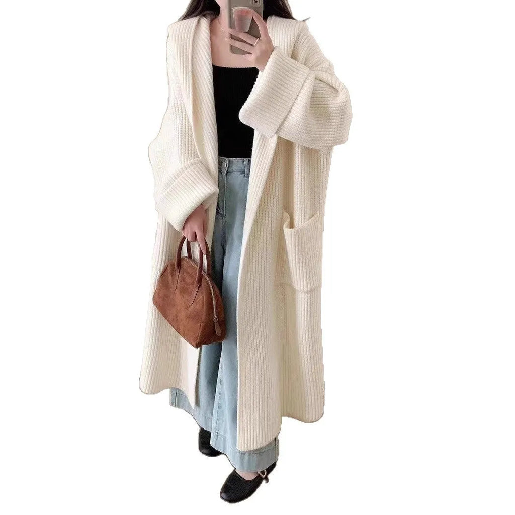 A woman wearing a long, loose, hooded cardigan coat in a neutral colour, showing its oversized fit and length.
