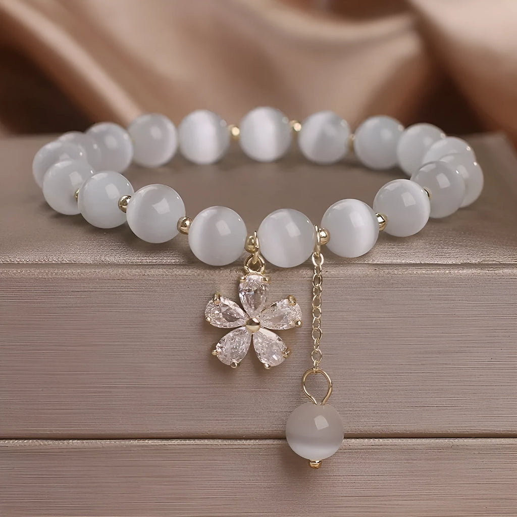 Women's white cat's eye stone bracelet with floral detail and a safety buckle pendant on a single loop.