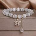 Women's white cat's eye stone bracelet with floral detail and a safety buckle pendant on a single loop.