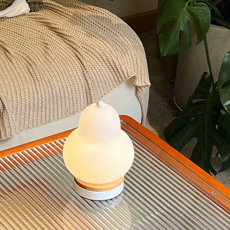 White pear-shaped rechargeable touch LED table lamp with PE shade on a wooden bedside table