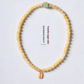 Close-up of a women's hand-woven bracelet with topaz-coloured barrel beads, square jade beads, and a fu charm.