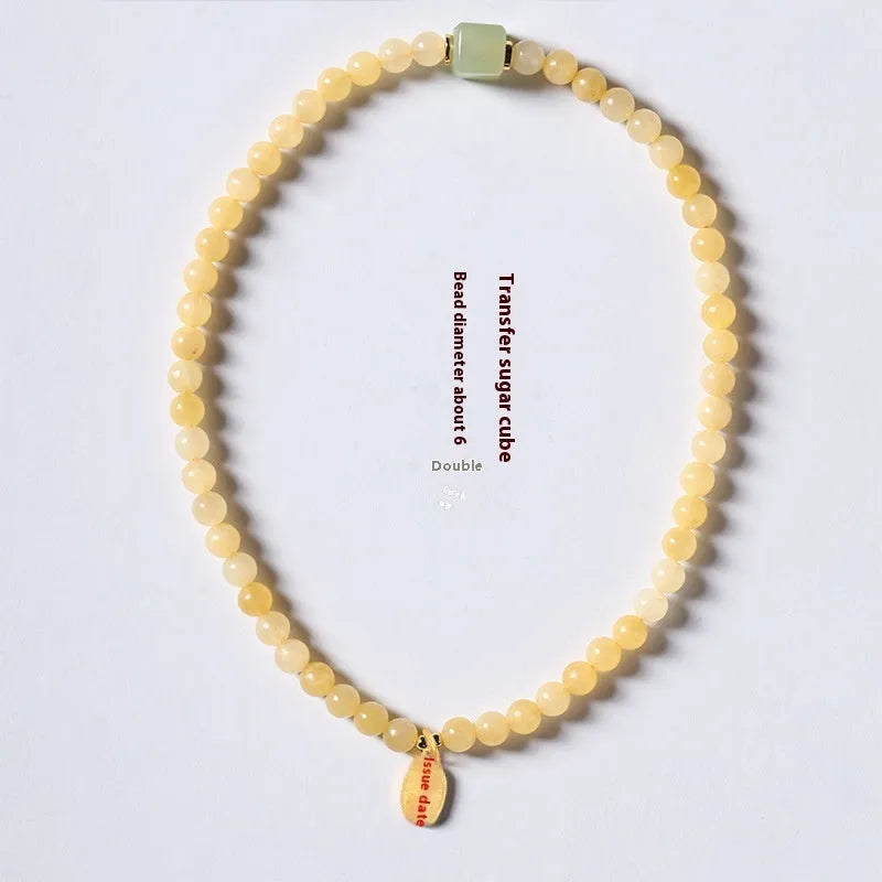 Close-up of a women's hand-woven bracelet with topaz-coloured barrel beads, square jade beads, and a fu charm.
