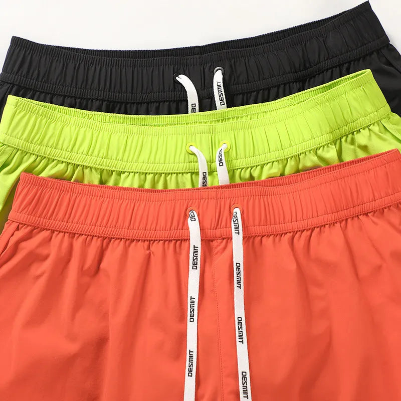 Man wearing loose orange red polyester shorts on a beach, showcasing the fit for surfing and leisure.