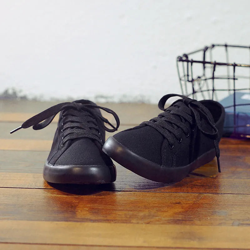 All black women's low-top canvas flat shoes with flat rubber sole and lace-up front.