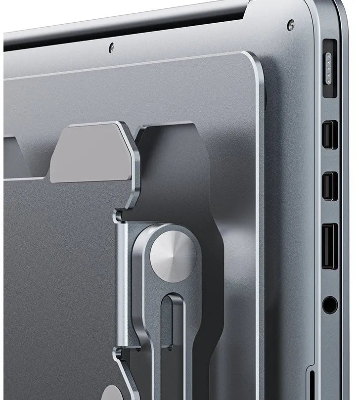 Grey aluminium laptop stand in a folded position next to an open laptop, showing its adjustable angle and hollow design.