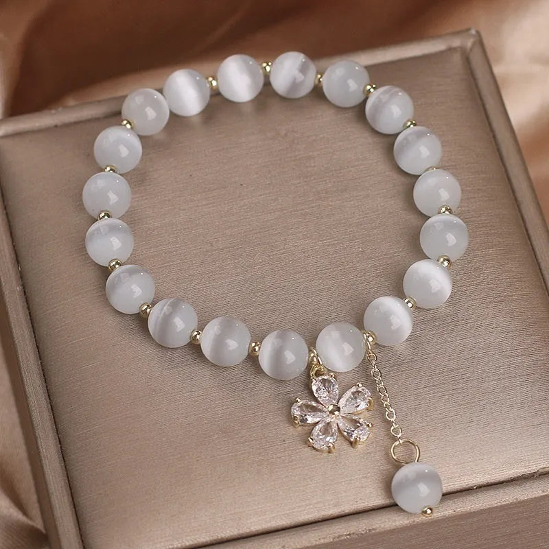 Women's white cat's eye stone bracelet with floral detail and a safety buckle pendant on a single loop.