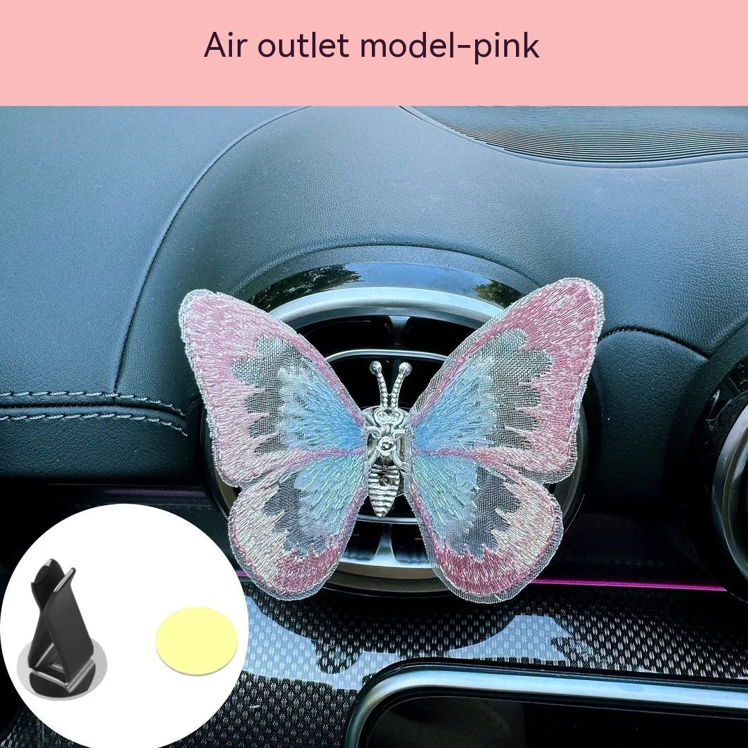 Soft fabric embroidered butterfly car air vent decoration in multiple colour options on a centre console.