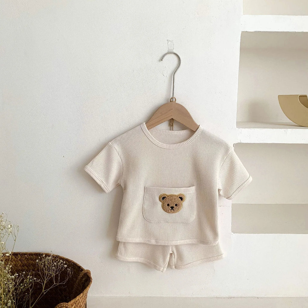 Unisex baby summer suit with bear print cotton top and beige shorts on a neutral background