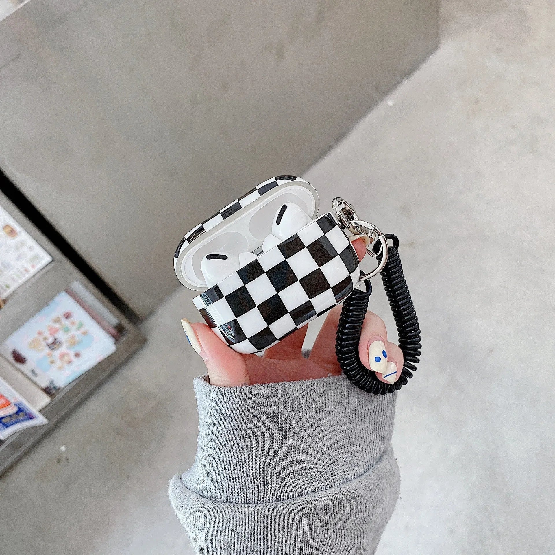 Black and green checkerboard pattern TPU protective case sleeves for Apple AirPods, one with a smiley face lanyard attached.
