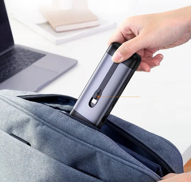 USB-C to multi-port docking station adapter with short cable shown next to a laptop, displaying HDMI, USB, and charging ports.