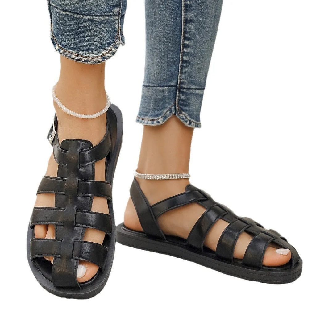 Flat Roman style women's sandals with buckle, black PU upper and rubber sole, side view