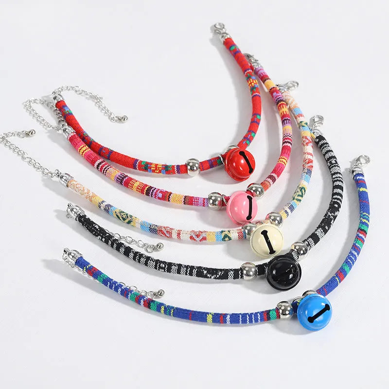 Coloured ethnic-pattern adjustable dog or cat collar with a small metal bell attached, shown in pink.