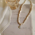 Gold electroplated adjustable vintage pearl necklace with a geometric charm on a black background.