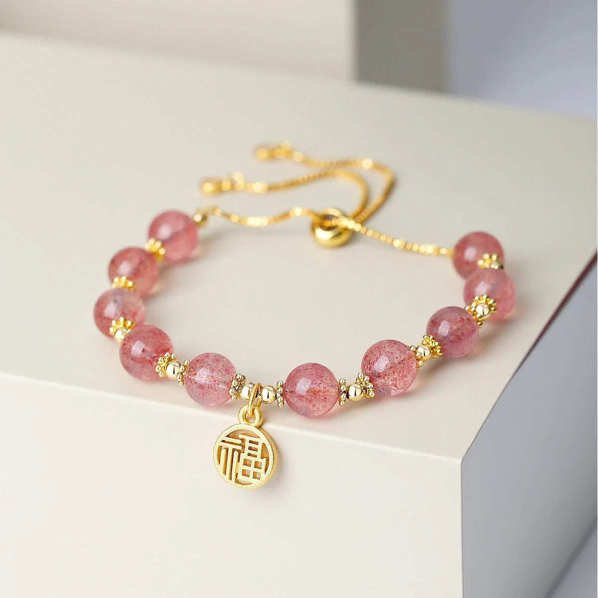 Women's strawberry quartz bracelet with geometric charms and fu character on wrist