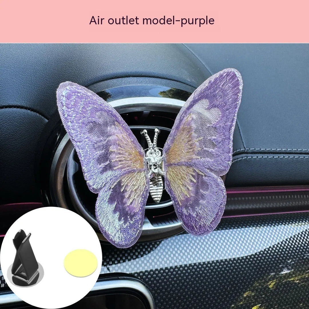 Soft fabric embroidered butterfly car air vent decoration in multiple colour options on a centre console.