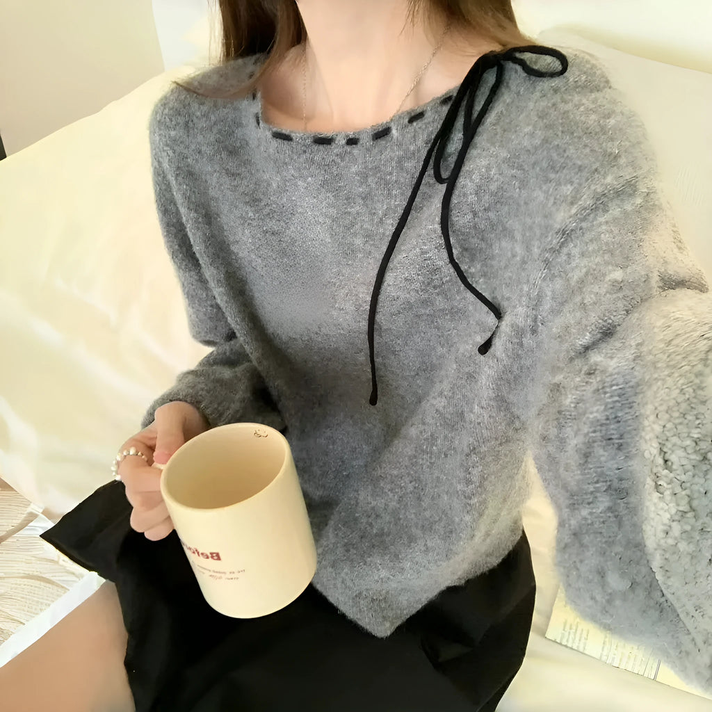 A grey women's loose-fitting knitwear pullover on a hanger, showing its casual style.