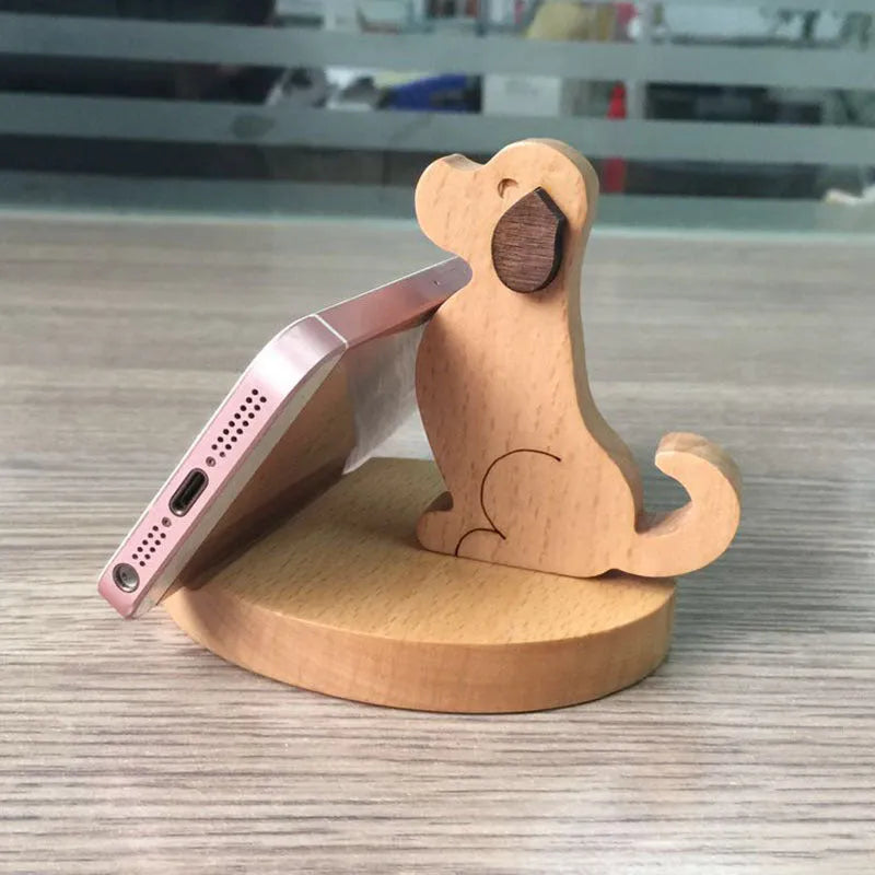 Solid beech wood phone stand with a decorative resin puppy figurine, holding a mobile phone at an angle with a charging cable threaded through the back.