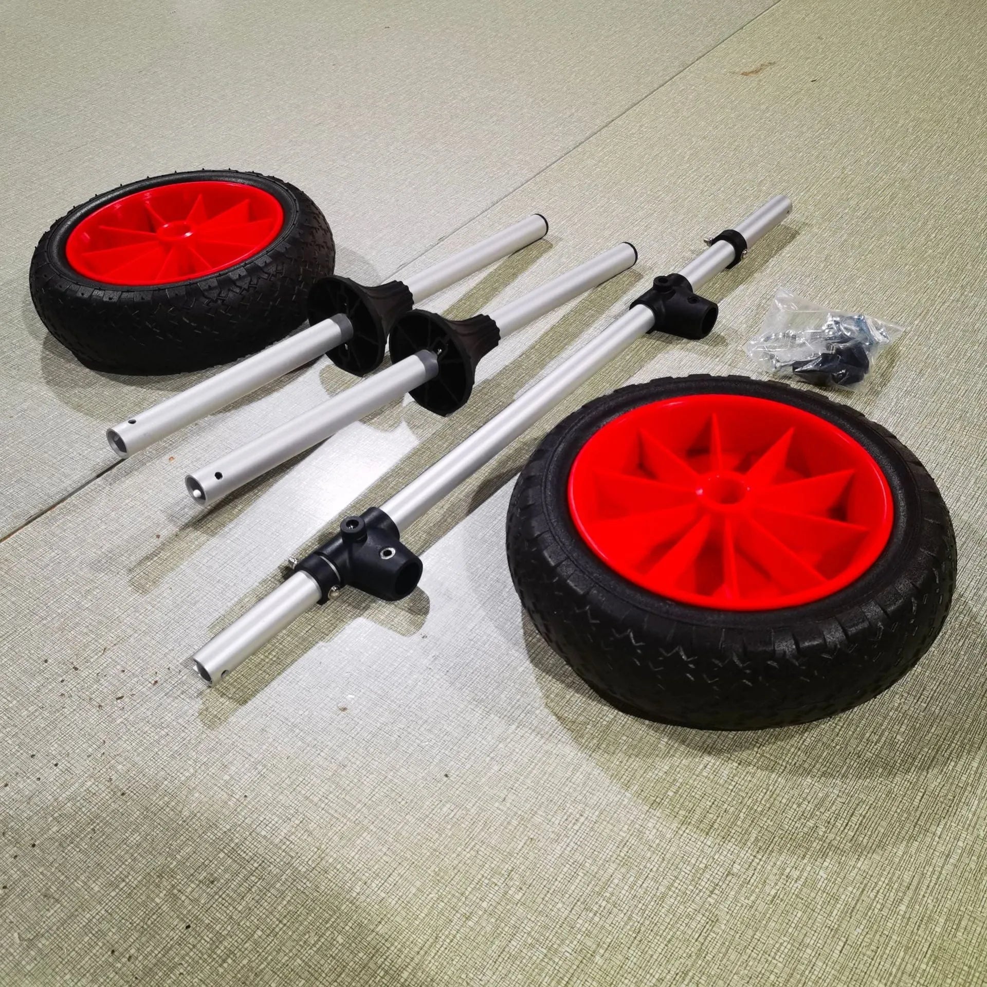 Foldable aluminium kayak handcart with large rubber wheels, shown carrying a yellow kayak on a beach.