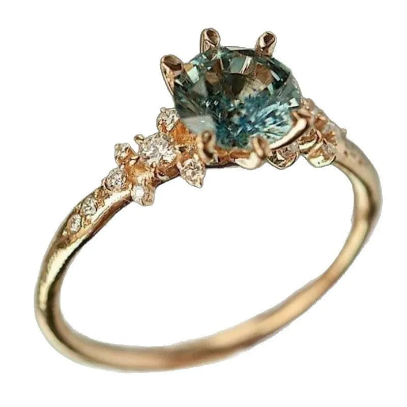 A gold-coloured geometric ring with a claw setting holding zircon stones on a chamfered square patterned band.