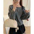 A grey women's loose-fitting knitwear pullover on a hanger, showing its casual style.