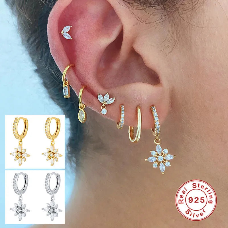 A pair of sterling silver snowflake pendant earrings with a gemstone, shown in yellow gold and white gold colour finishes.