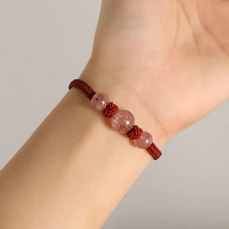 A woven red rope bracelet with a natural strawberry quartz bead and an alloy clasp.