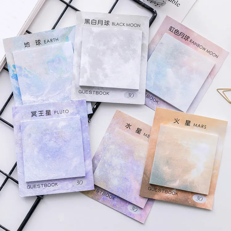 Square sticky notes notepad open to show planet oil painting designs including Earth and Rainbow Moon.