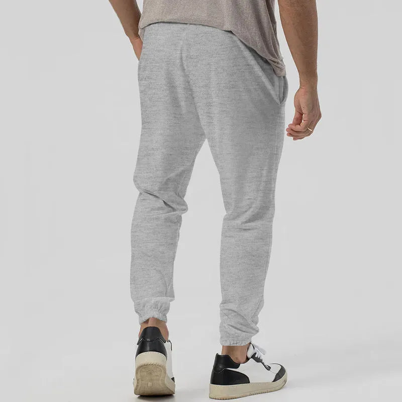 Men's grey straight-leg track sweatpants with a mid-waist, showcasing a relaxed fit and casual style.