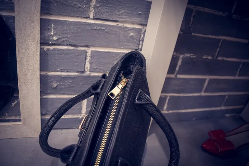 Women's PU messenger bag in black with zipper pocket and shoulder strap, top view with mini iPad inside.